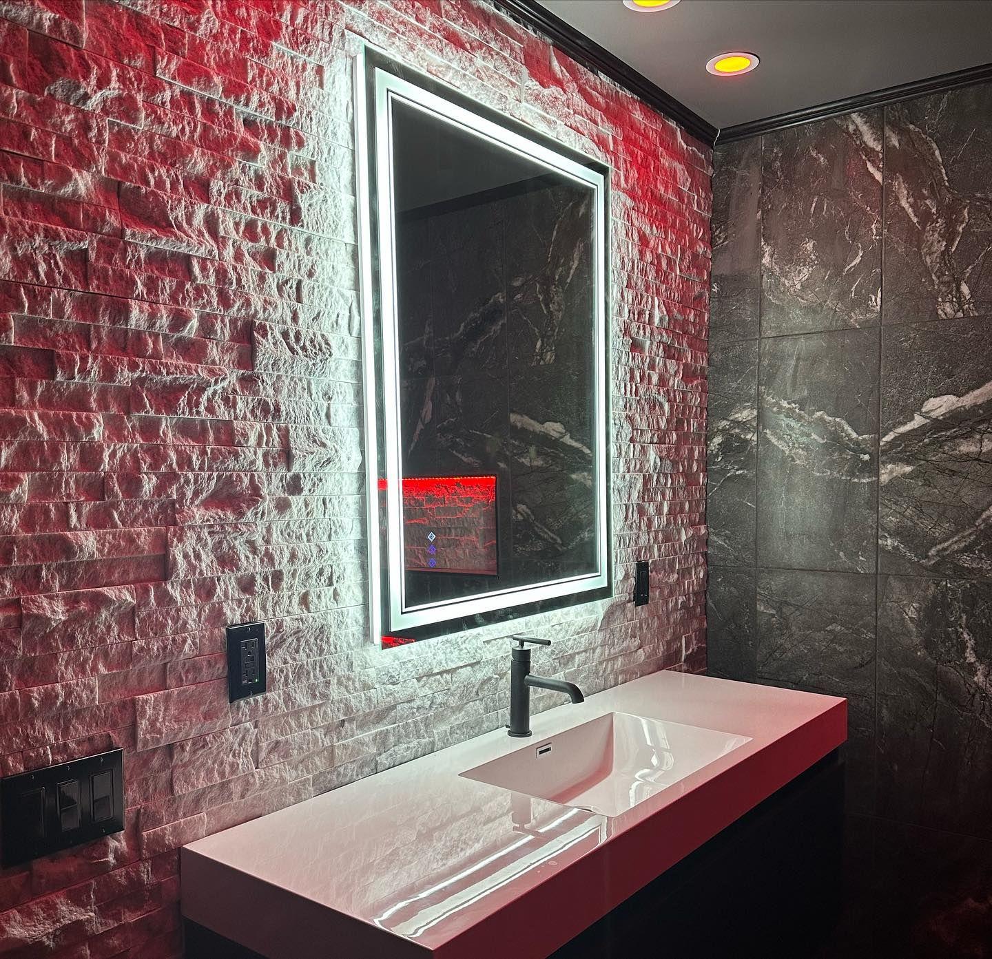 Modern bathroom with a white countertop sink, illuminated mirror, textured wall, and red accent lighting.